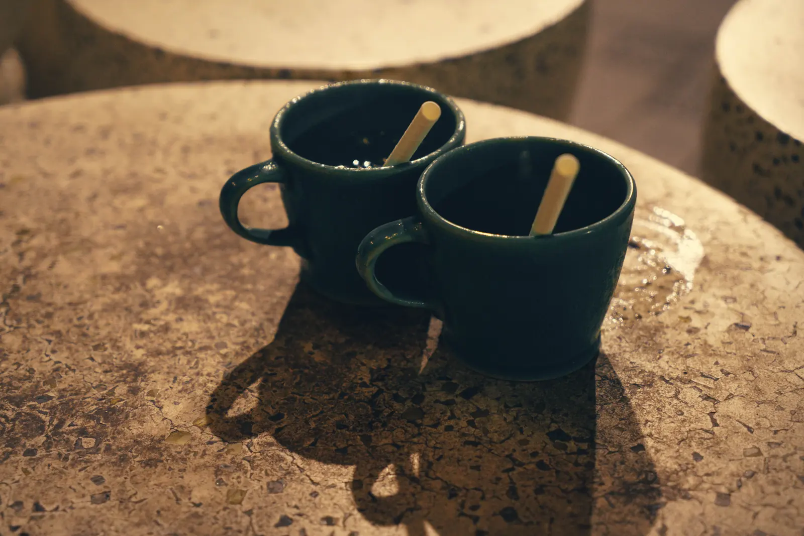 Two empty green mugs side by side on a stone table in low afternoon light